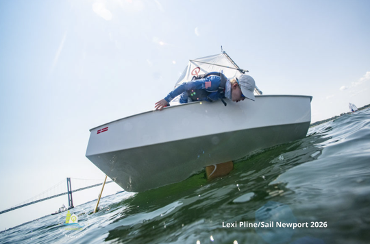 A person leans over the edge of a small sailboat, touching the water. A bridge is visible in the background under a bright sky. Text on the image reads “Lexi Pline/Sail Newport 2026.”.
