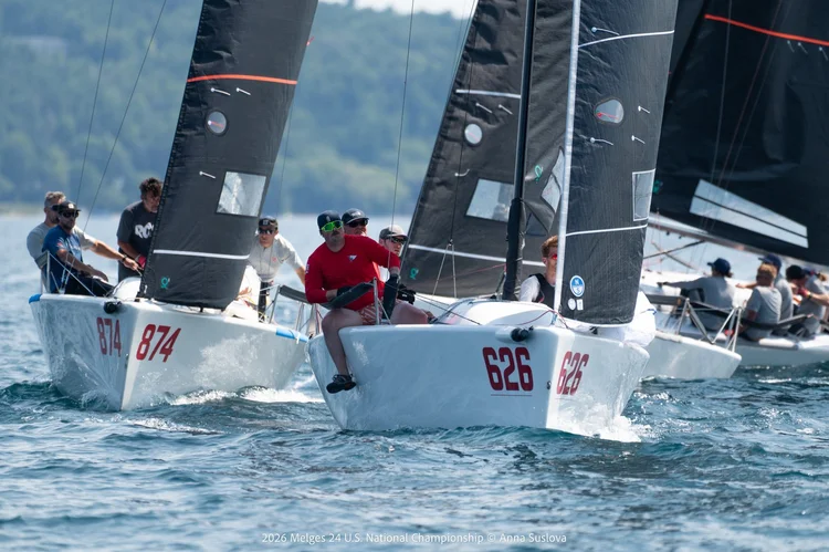 Sailboats with crews compete in a race on a sunny day, with boat numbers 874 and 626 visible at the front, and more boats and water in the background.