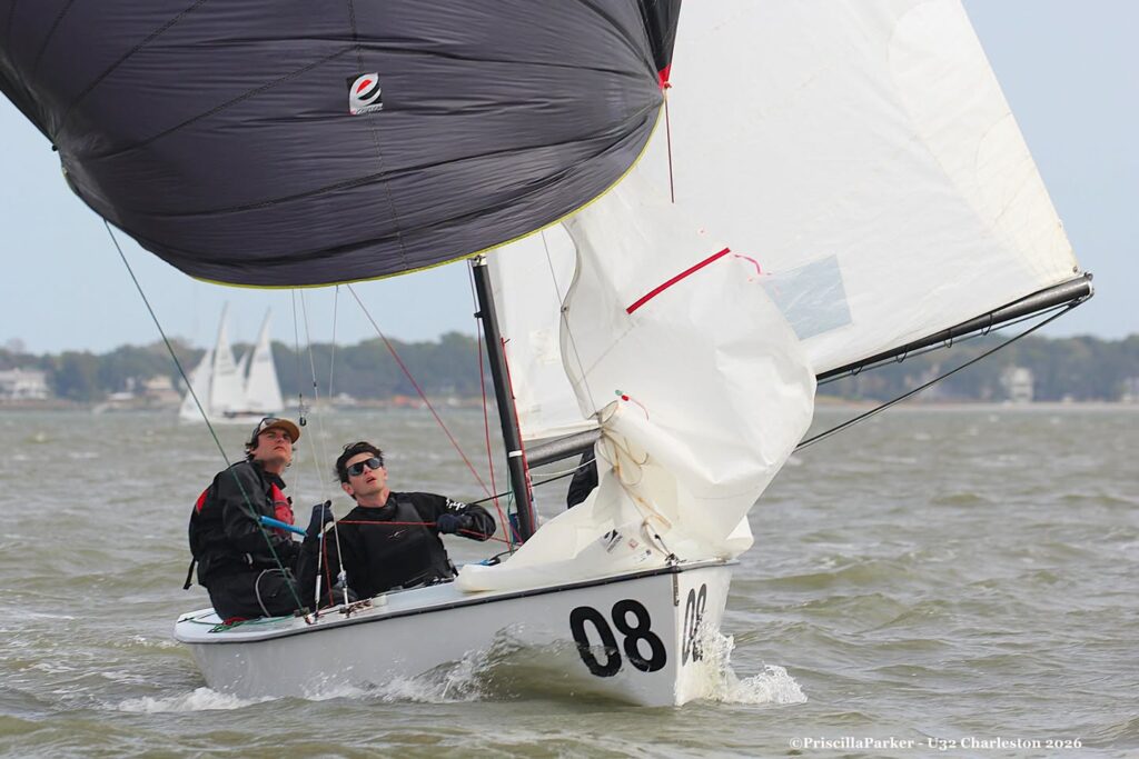 Two people sailing a small white sailboat with a large black spinnaker sail and the number 08 on its hull.