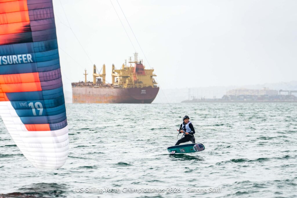A kiteboarder at the US Sailing Youth Championships with a large cargo ship in the background.
